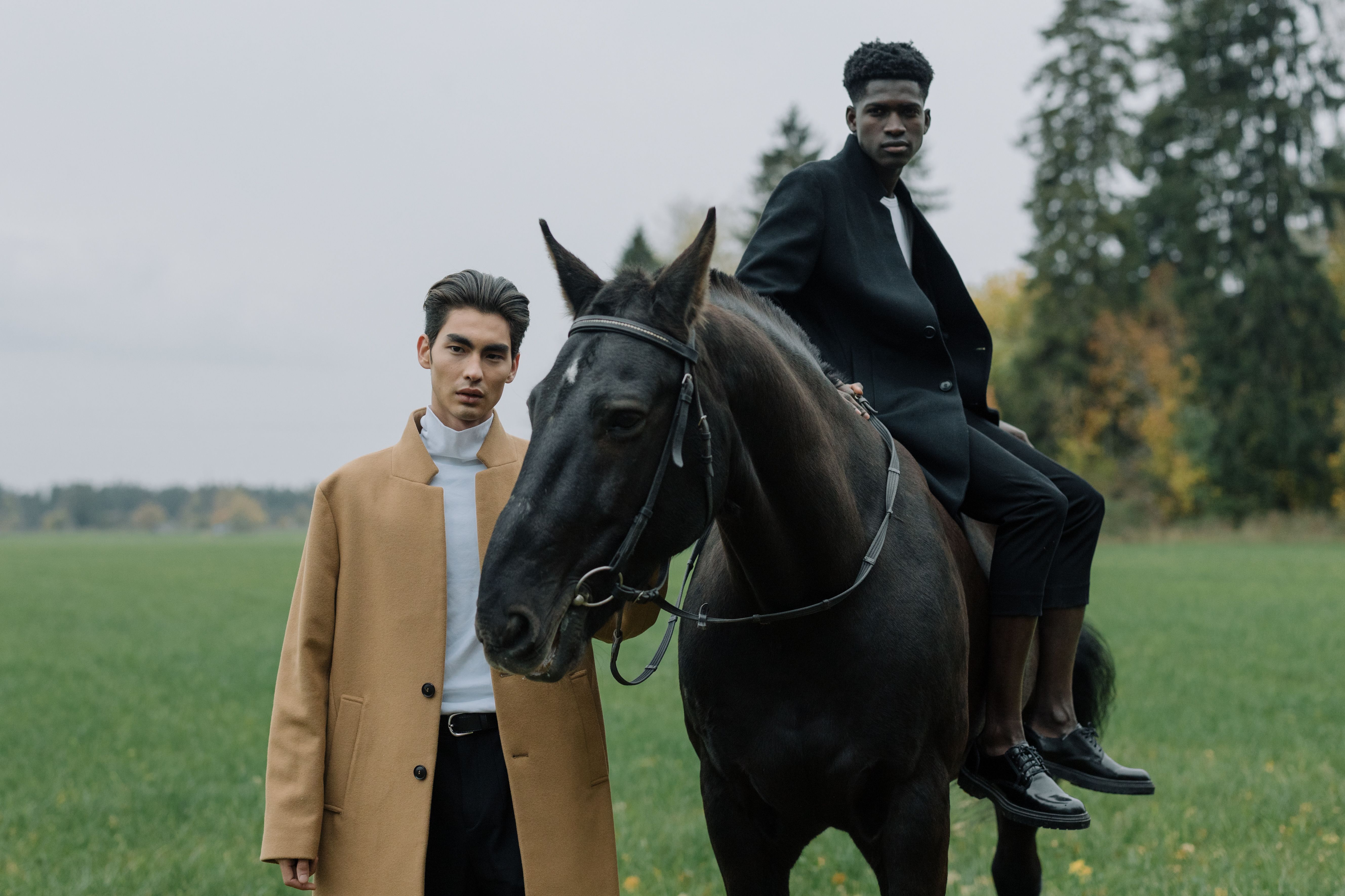 Zwei Models in Mänteln auf einem Feld, einer auf einem Pferd